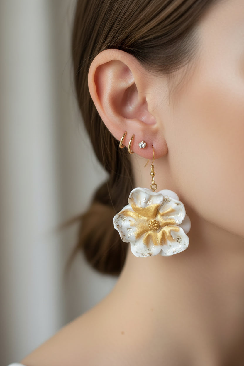 Ces boucles d'oreilles présentent un motif floral raffiné en blanc immaculé, rehaussé de touches dorées pour une touche de sophistication. L'argile polymère utilisée garantit une légèreté exceptionnelle tout en offrant une résistance durable