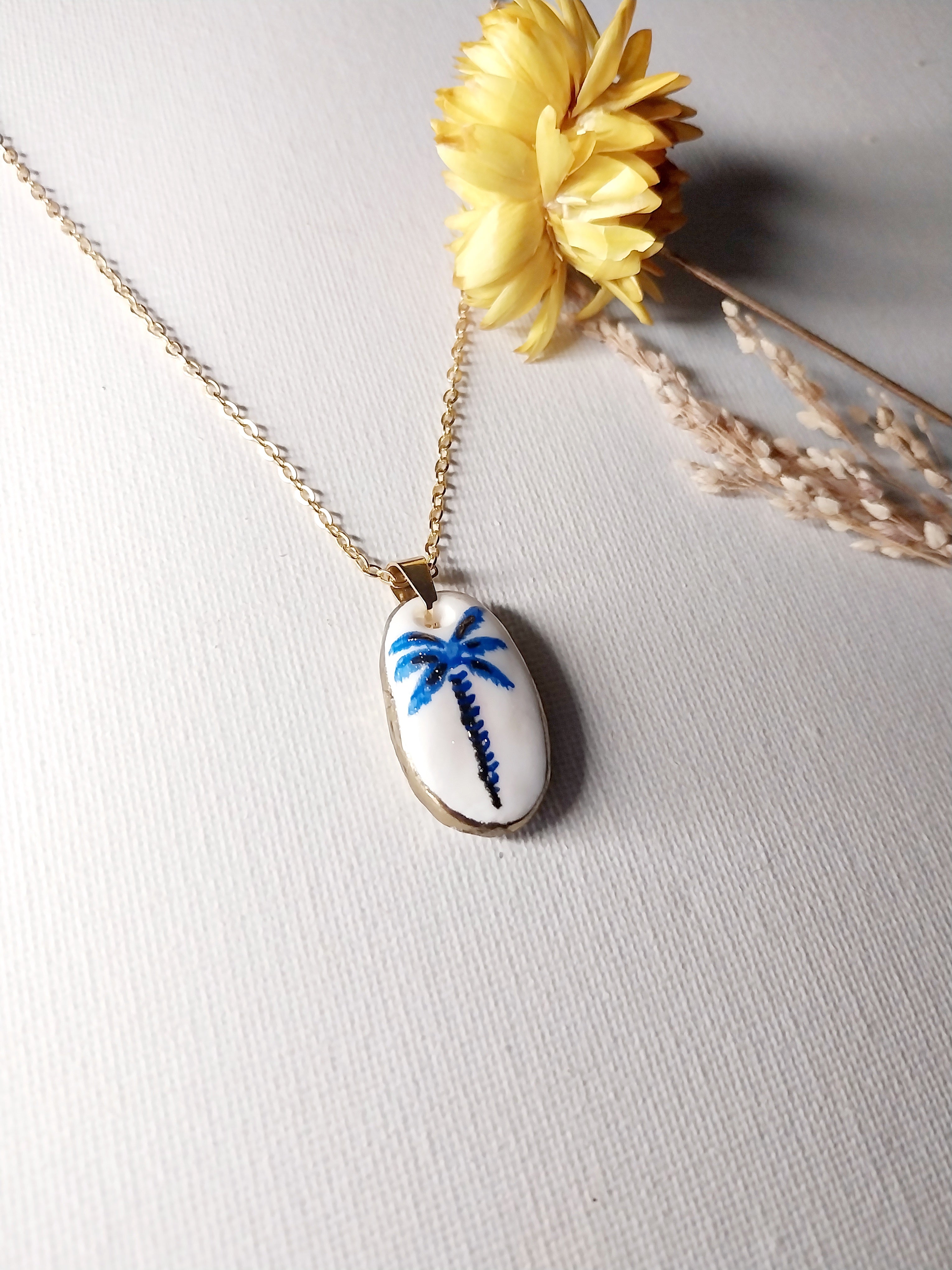 Pendentif artisanal palmier bleu et doré en argile polymère sur fond blanc